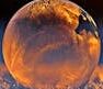 Close-up shot of a frozen bubble with warm reflections resting on a snowy surface at twilight.